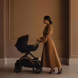 a woman in beige jacket next to a black stroller