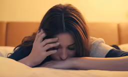a girl in bed is holding her hand on her head