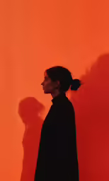 a woman with hair in a pony tail, standing against an orange wall