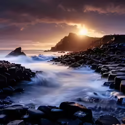 the sun setting over some rocks near the ocean