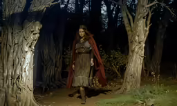 woman in dress and cloak walking through dark forest