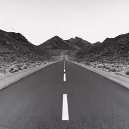 an empty road in a desert with mountains in the background