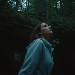 a woman looks up into the dark in the forest
