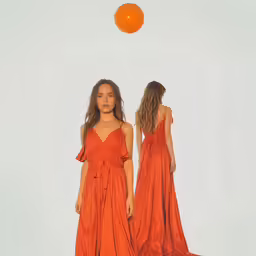 two woman are in orange dresses on the runway