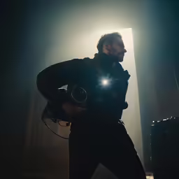a man with an electronic device stands in a stage light