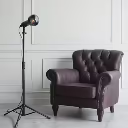 a large brown chair and a tripod light in front of a white wall