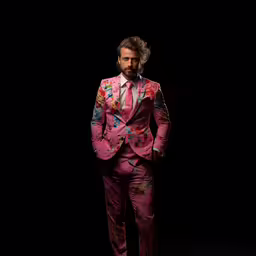 a man wearing a pink suit and tie,a man wearing a suit and tie while standing in a dark room