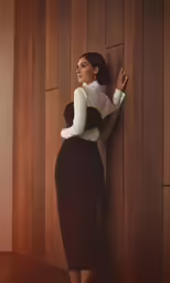a woman leans against the wall wearing a skirt