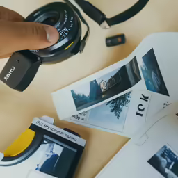 a hand holding up a camera over some pictures