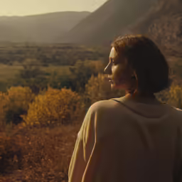 a woman stares toward a field and mountains