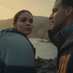 a man and woman look out at the water in a landscape
