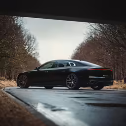 a black car driving on a paved road next to trees