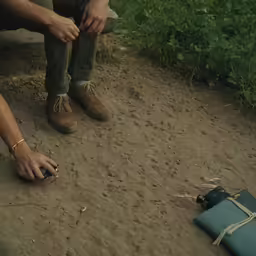 a person squatting on a dirt floor next to a blue suitcase