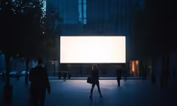 two people walk by a large screen in an empty plaza