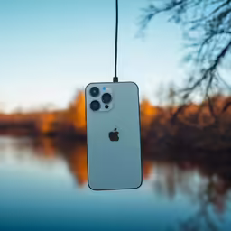 a white apple phone hangs over a lake