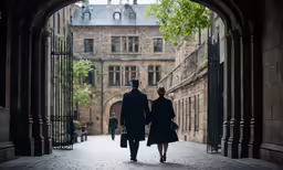 two people walking through a stone courtyard with an iron gate