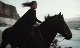 woman riding horse near body of water in mountainous area