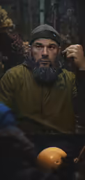 a man sitting with a hat on while he puts on a beard