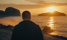 a man watching the sun set by the water