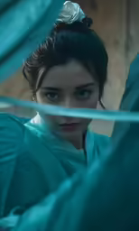 a girl in a green kimono poses in front of blue curtains
