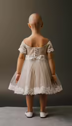 a child is wearing a wedding dress that has lace overlays and bows