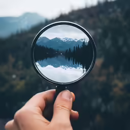 someone holding up a small mirror to the camera with a reflection of mountains in it