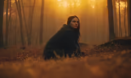 a girl is sitting in the grass in front of a forest