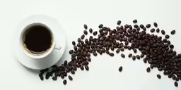a white cup with coffee beans and saucer