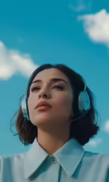 woman with blue sky background wearing white headphones
