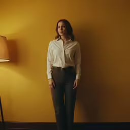 a young lady in white shirt and green pants standing next to yellow wall