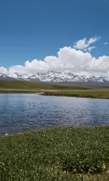 the green hills have snow - capped mountains in the distance