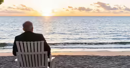 an older man sitting on a lawn chair on the beach
