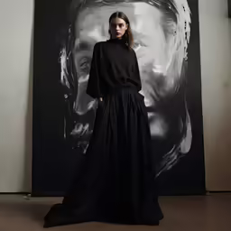 model in black gown and headdress next to a large canvas portrait