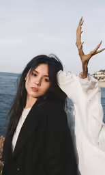a woman stands with her arm extended wearing a black coat
