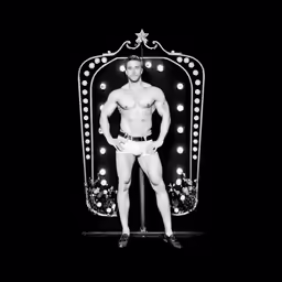 naked man posing on stage with neon sign behind him