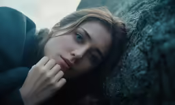 a woman leaning on the side of a stone wall