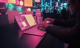 the man is holding a cell phone next to his laptop