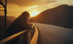 a woman sitting on the side of a road while watching the sunset