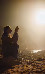a girl kneeling on the sand with her arms in the air and outstretched hands