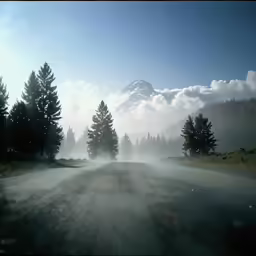 a long straight road with mist and a snow - capped mountain in the background