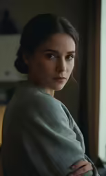 a woman is standing in front of the window with her arms crossed
