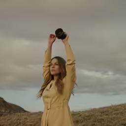 a woman in a yellow dress holding up a hat