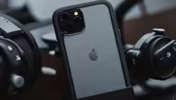 a black iphone sits next to headphones and a camera