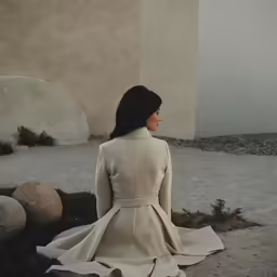 a woman sitting on the ground in a trench coat