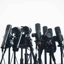 multiple cameras and tripods sitting up against the sky