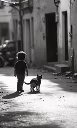 small child is walking beside a black and white cat