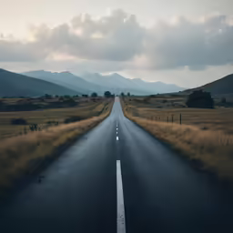 the empty highway in front of a field with mountains