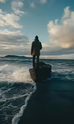 person standing on rock in front of waves looking at shore