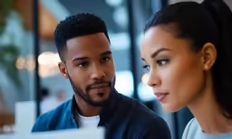 a beautiful woman standing next to a man who is using a computer