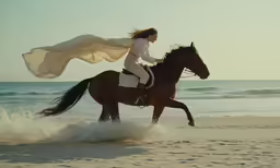 a woman in white riding a horse down the beach